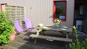 Een houten picknicktafel met een bank, een paarse stoel en een bloempot met plant.