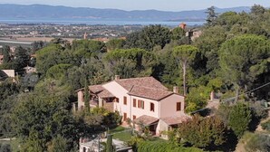 A house with a tiled roof, surrounded by trees and a view of a distant town and mountains.