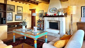 A cozy living room with a fireplace, wooden beams, and a bookshelf.