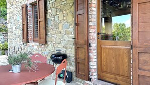 A stone building with a wooden door and window shutters, a round table with chairs, and a potted plant.
