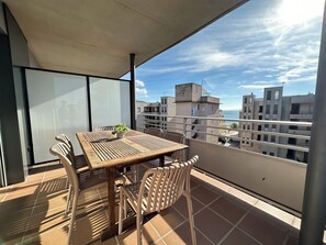 Un balcon avec une table et des chaises en bois, un pot de fleurs et une vue sur les bâtiments et la mer.