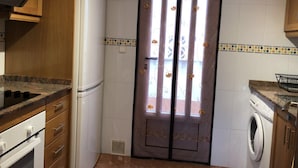 A compact kitchen with a refrigerator, stove, oven, and a washing machine. - BUNGALOW WITH TERRACE 50M2,500M TO THE BEACH (Los Arenales del Sol)