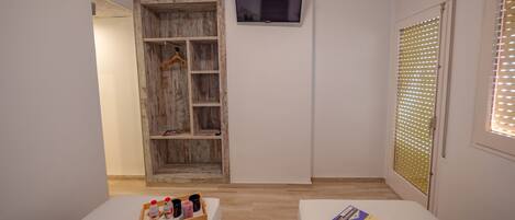 Una habitación con un armario de madera, un televisor montado en la pared y una ventana con persianas.