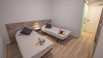 Een kleine, moderne kamer met twee eenpersoonsbedden, een houten hoofdbord, een nachtkastje met een lamp en een klein tafeltje met dienblad.
