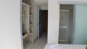 Une chambre d’hôtel avec une armoire en bois, une douche en verre et un lit blanc.