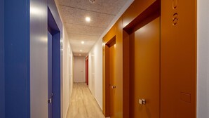 A hallway with wooden flooring, blue and orange doors, and a ceiling with recessed lighting. - Agi Gloria Rooms 304 Hostel for rent in Roses Girona. (Roses)