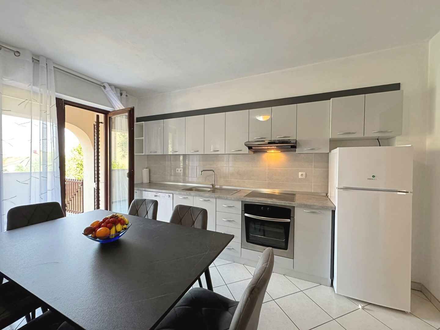 Une cuisine moderne avec des meubles blancs, un plan de travail noir et un réfrigérateur blanc.