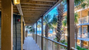 Eine Holzterrasse mit Geländer, die auf einen Strand und Palmen blickt.