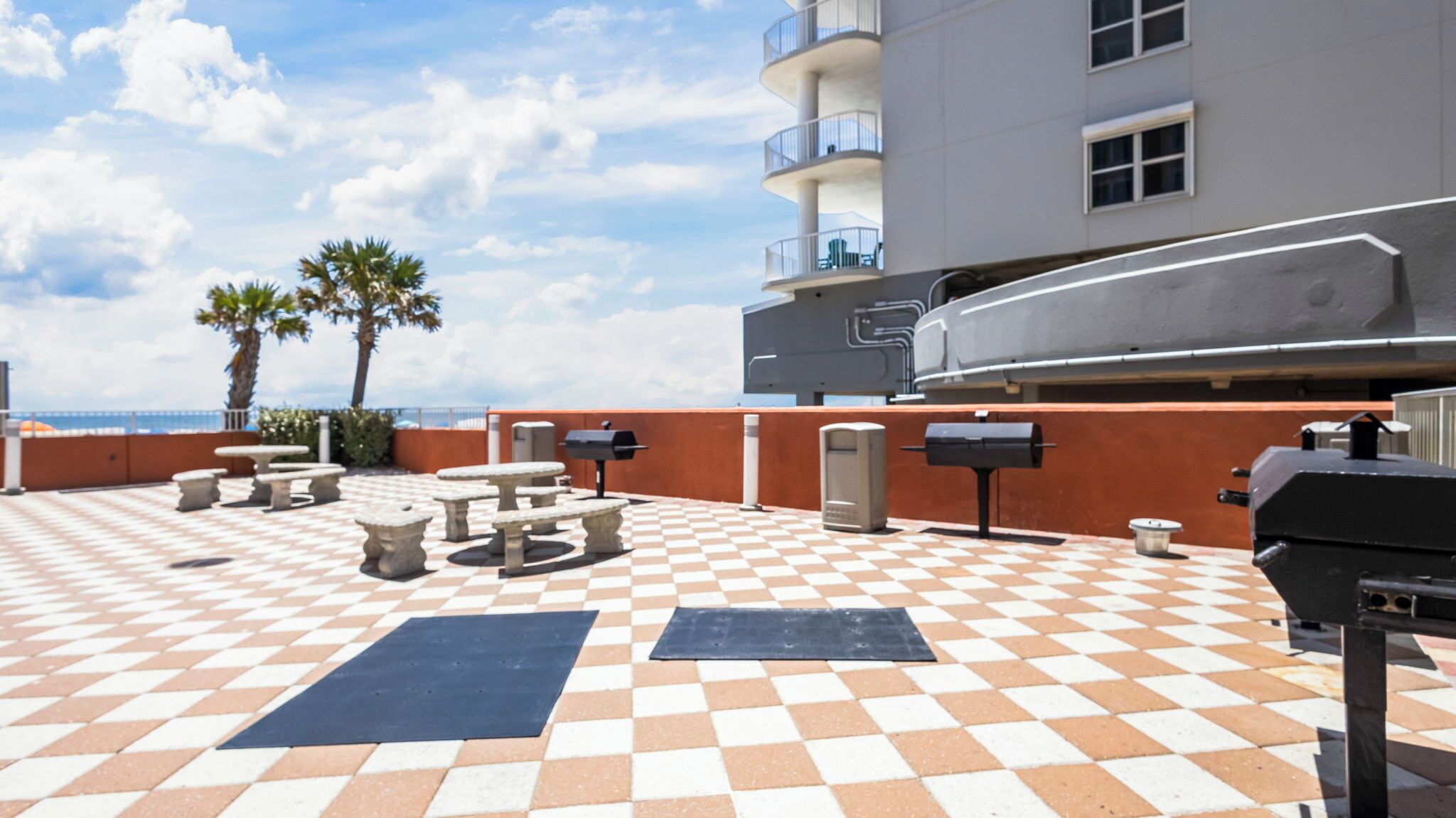 Une terrasse extérieure avec un sol à carreaux, des sièges et un barbecue.