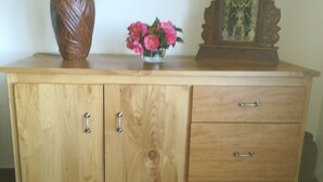 Un meuble en bois avec deux portes et un tiroir, une lampe et un vase rempli de fleurs.