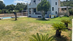Une maison à deux étages avec une piscine, un patio couvert et un mur en pierre.