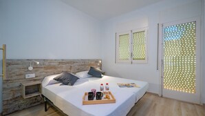 A modern bedroom with a wooden headboard, a bedside table with a lamp, a bed with pillows, a tray with breakfast items, and a window with a patterned blind. - Agi Gloria Rooms 202 Hostel for rent in Roses Girona. (Roses)