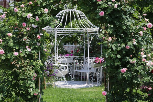 Un belvédère à la structure métallique blanche, entouré d’un feuillage verdoyant et de roses roses.