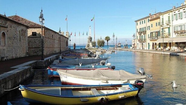 A marina with boats docked along a waterfront, buildings with balconies, and a clear sky. - DREAM HOLIDAY ON LAKE GARDA (Lazise)
