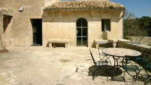 A rustic building with a tiled roof, a stone bench, and a round table with chairs.