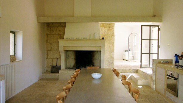 A long dining table with chairs, a fireplace, and a kitchen area with cabinets and appliances.
