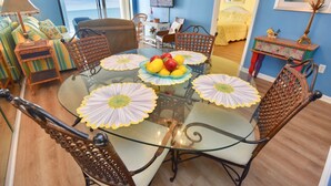 Un coin repas avec une table en verre entourée de chaises en osier, un canapé et un téléviseur en arrière-plan.