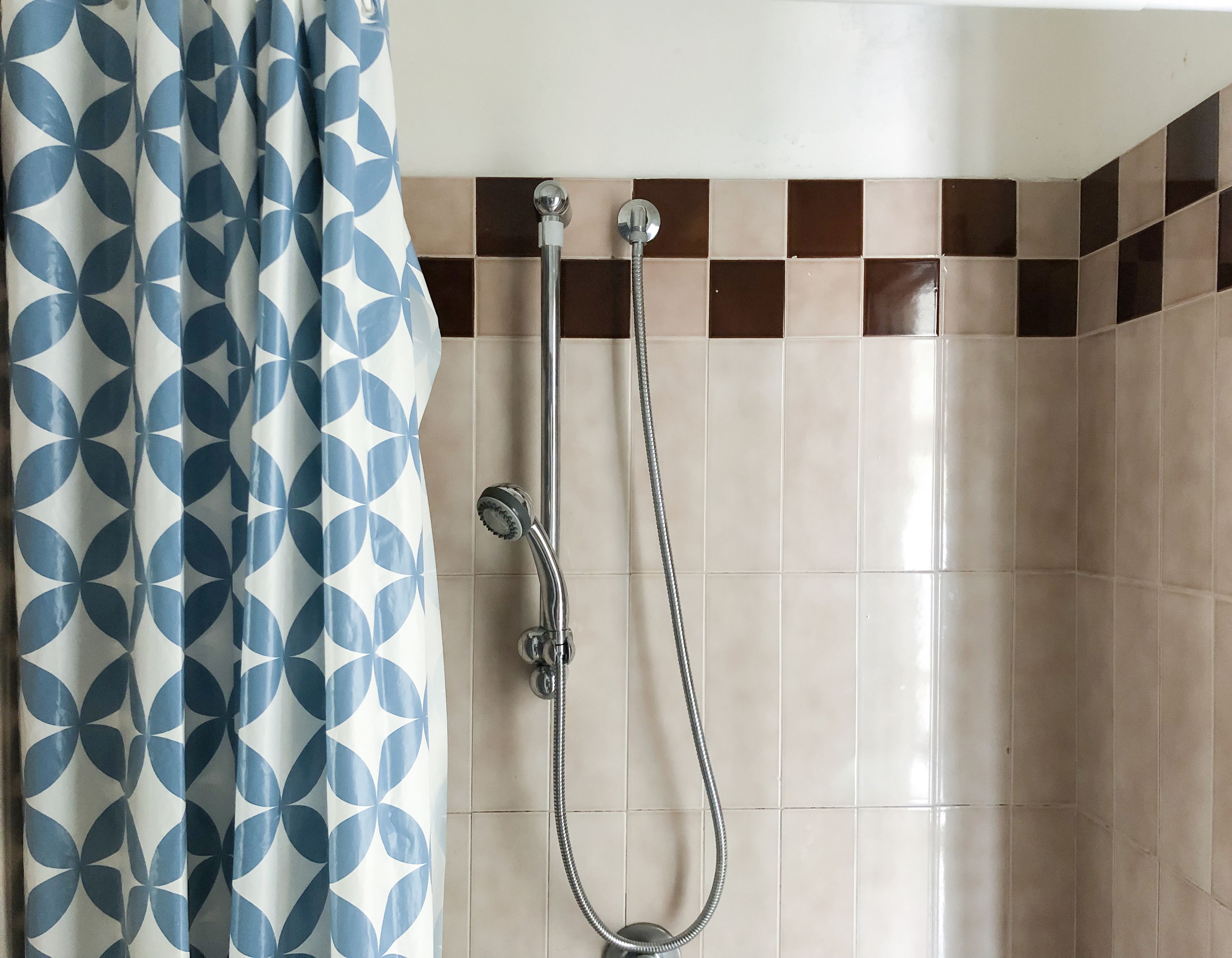 A shower with a handheld showerhead and a wall-mounted faucet, a curtain with a geometric pattern, and a tiled wall with a checkered design.