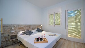 Une chambre moderne avec une tête de lit en bois, une table de chevet avec une lampe, un lit avec des oreillers, un plateau avec des éléments de petit-déjeuner et une fenêtre avec un store à motifs.