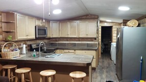 A compact kitchen with wooden cabinets, a microwave, a sink, and a refrigerator. There are three wooden stools at the kitchen island.