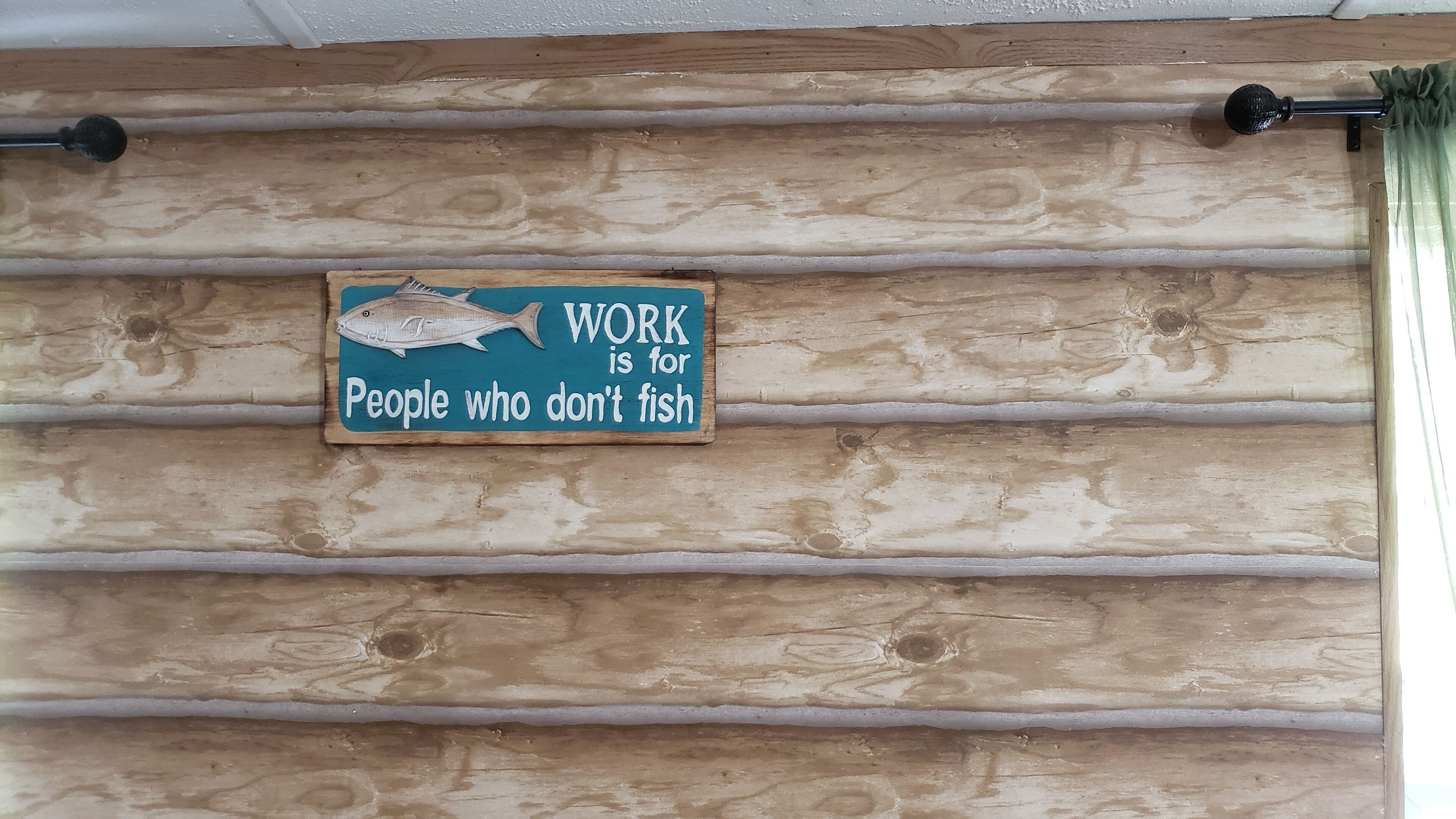 A wooden wall with horizontal planks and a sign that reads 'WORK is for People who don't fish.'