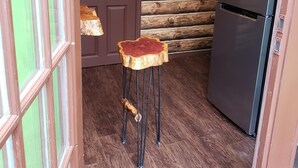 A wooden log wall, a refrigerator, and a wooden stool in a kitchen.