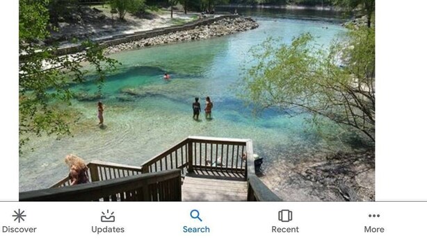 A river with clear water, a wooden deck, and people standing by the water.