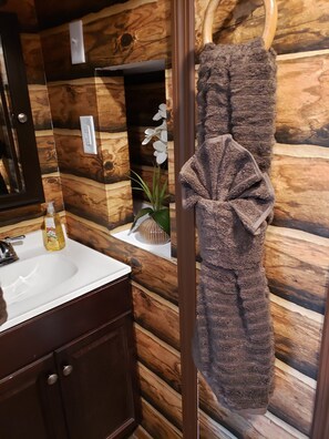 A bathroom with a wooden wall design, a sink with a bottle of hand soap, and a towel hanging on a hook.