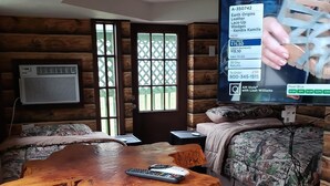 A cozy log cabin room with a wooden dining table, a television, and a bed with camouflage bedding.
