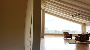 Il s’agit d’une pièce spacieuse dotée d’un plancher en bois, de grandes fenêtres et d’un plafond avec des poutres apparentes. On y trouve deux fauteuils et une petite table.