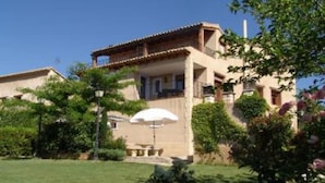 A two-story building with a balcony and a covered outdoor seating area. - Asque: House with garden (Asque)