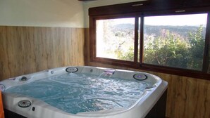 A hot tub in a room with wooden walls and a window overlooking a mountainous landscape. - Asque: House with garden (Asque)