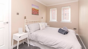 A bedroom with a white bed, a nightstand, a painting, and two windows. - The Cluthar: Ground Floor West End /City Centre / Rockvilla Flat & Parking (Glasgow)