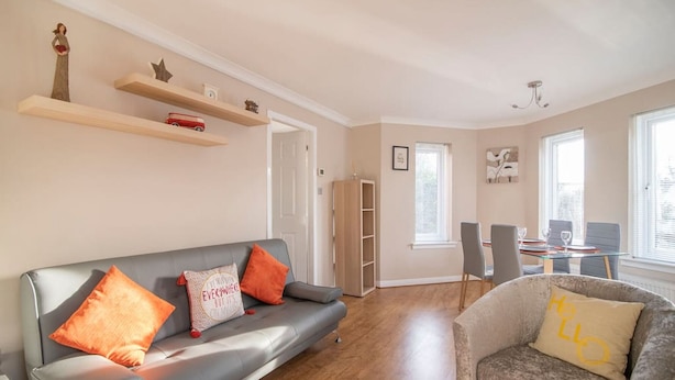 A living room with a grey sofa, a chair, a dining table with chairs, a bookshelf, and a window. - The Cluthar: Ground Floor West End /City Centre / Rockvilla Flat & Parking (Glasgow)