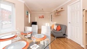 A modern living room with a glass dining table, grey sofa, and a white door. - The Cluthar: Ground Floor West End /City Centre / Rockvilla Flat & Parking (Glasgow)