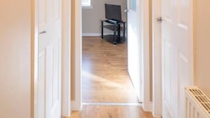 A hallway with white doors leading to a room with a wooden floor and a black chair. - The Cluthar: Ground Floor West End /City Centre / Rockvilla Flat & Parking (Glasgow)
