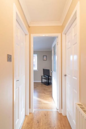 A hallway with white doors leading to a room with a wooden floor and a black chair. - The Cluthar: Ground Floor West End /City Centre / Rockvilla Flat & Parking (Glasgow)