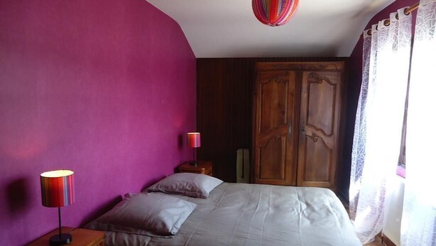 Une chambre à coucher avec un lit, une table de chevet avec une lampe, une armoire en bois et une fenêtre avec des rideaux.