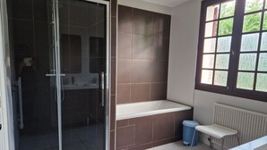 Une salle de bain moderne dotée d’une douche à parois de verre, d’une baignoire et d’une fenêtre avec du verre décoratif.