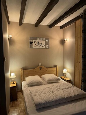 Ein Schlafzimmer mit einem Holzkopfteil, zwei Nachttischlampen, einem Bett mit weißer Bettwäsche und einem an der Wand hängenden Kunstwerk mit dem Wort 'HOPE'.