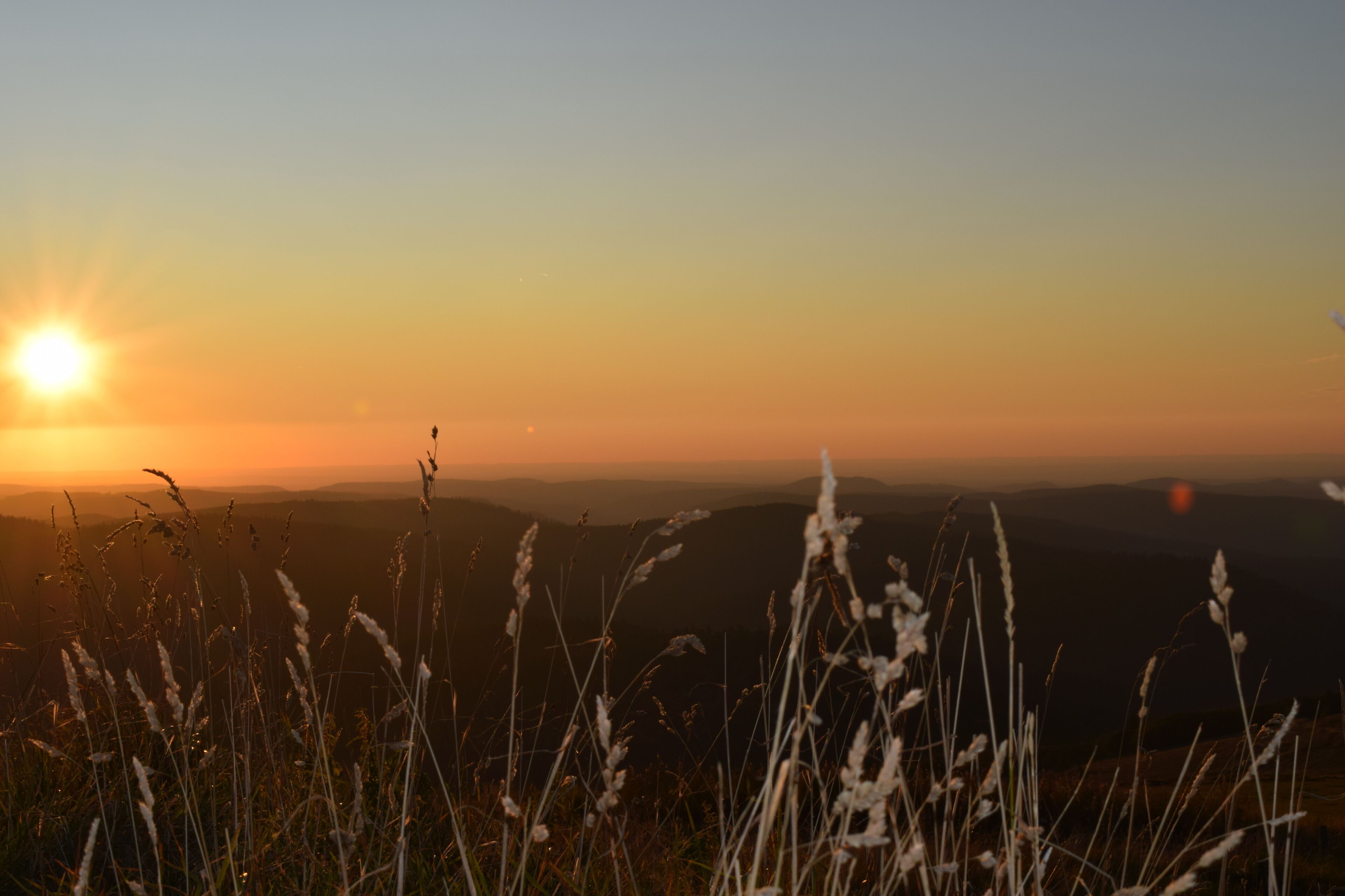 A sunset over a mountainous landscape with grass in the foreground.