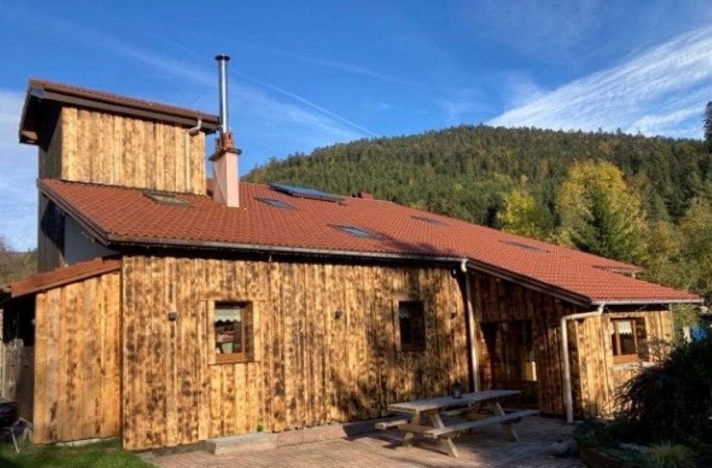 A rustic wooden building with a red-tiled roof, a chimney, and a picnic table outside.