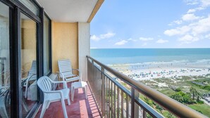 A balcony with white chairs and a view of a beach with umbrellas and people. - Family Fun at this Beachside Resort in Myrtle Beach (Myrtle Beach)
