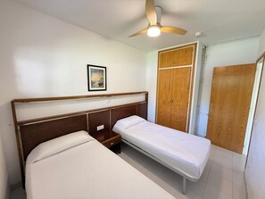 A bedroom with two single beds, a wooden wardrobe, a ceiling fan, and a framed picture on the wall.