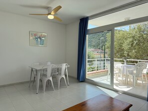 Ein Zimmer mit Esstisch und Stühlen, einem Deckenventilator, einem großen Fenster mit Balkonblick und einem Gemälde an der Wand.