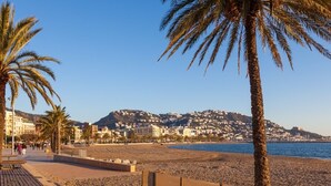 Een strand met palmbomen, een promenade en gebouwen op de achtergrond.
