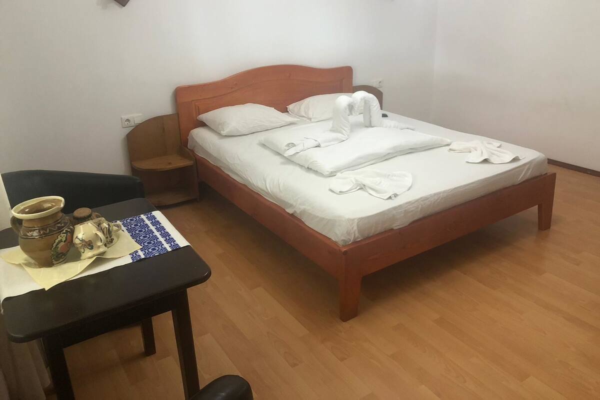 A neatly made bed with white linens, a wooden headboard, and a bedside table with a ceramic jug and a small pitcher.