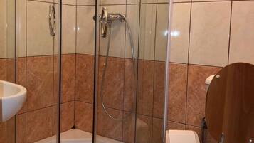 Un baño con ducha de vidrio, lavamanos blanco y inodoro de madera.