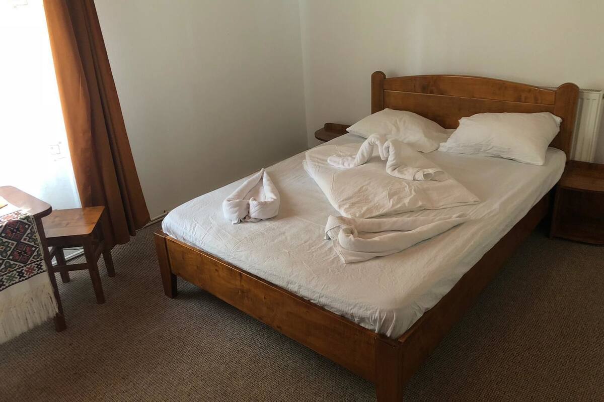 A single bed with a wooden headboard, a small wooden nightstand, a chair, and a patterned tablecloth.