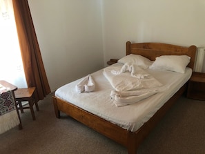 A single bed with a wooden headboard, a small wooden nightstand, a chair, and a patterned tablecloth. - Complex Turistic Alpina Blazna (Sant)